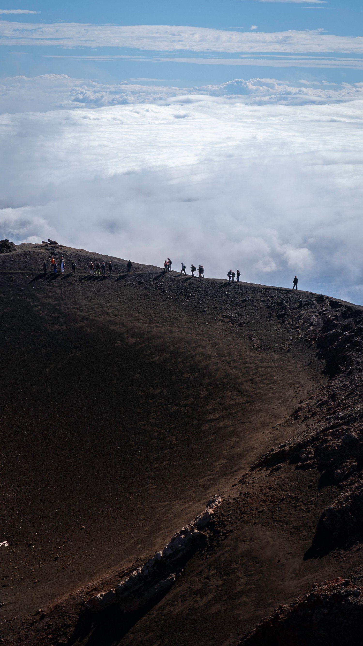 Hikers on the crater of Etna above the clouds, Sicilian volcanic landscape.