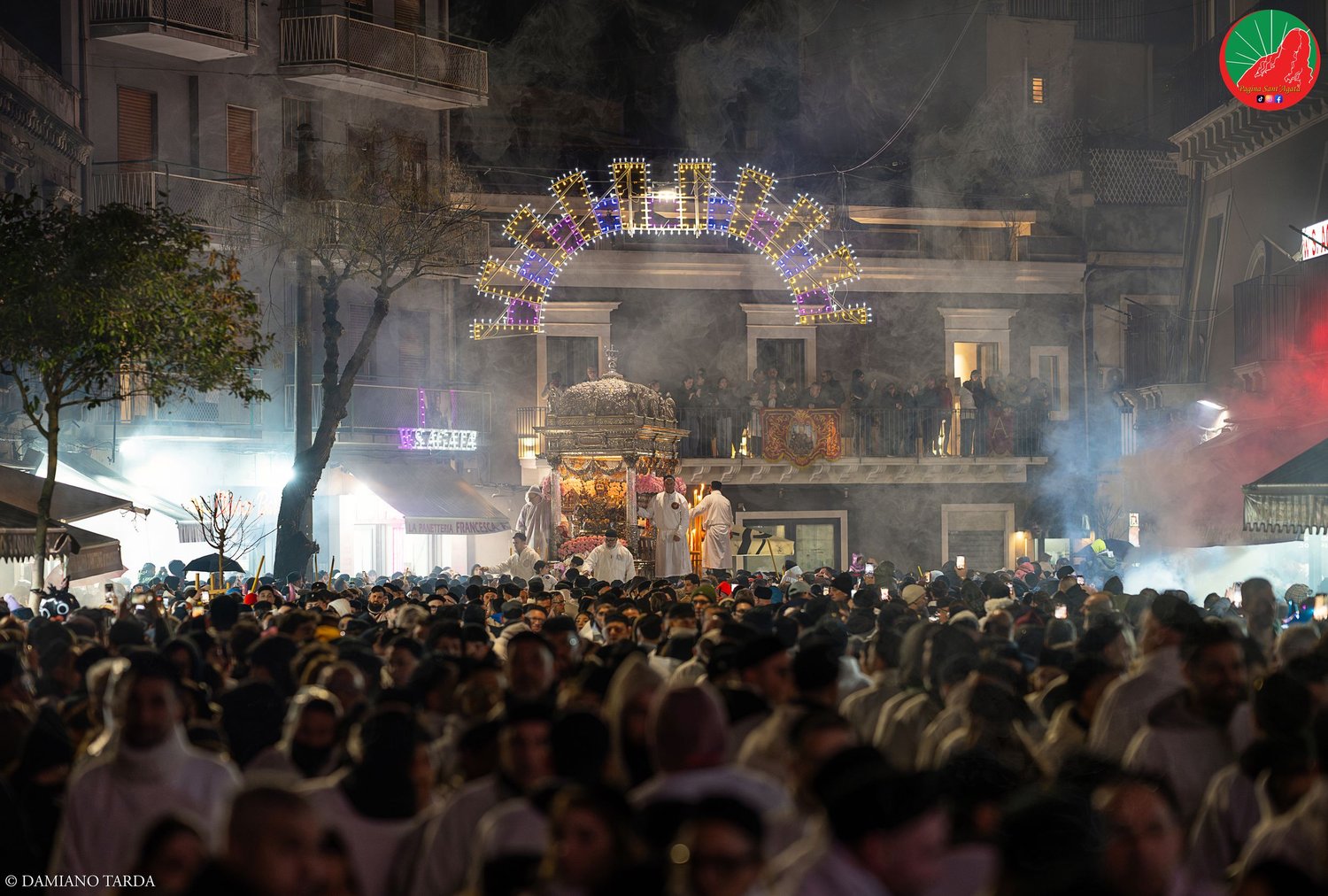 Crowd of devotees at night during the Feast of Saint Agatha, with the festival lights in the background.