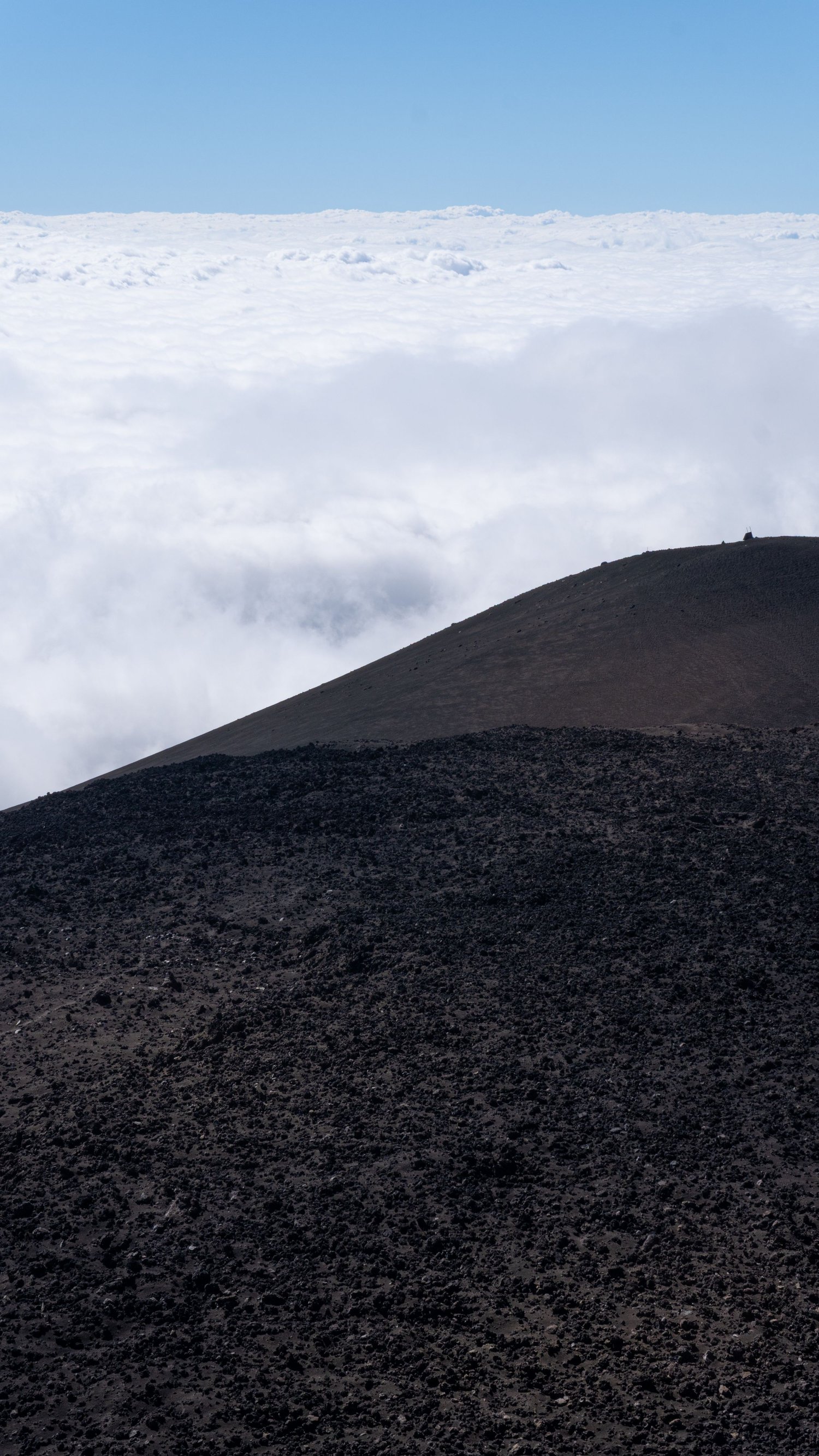 Calm, reflective landscape photography. The crater of Etna with clouds in the sky behind.
