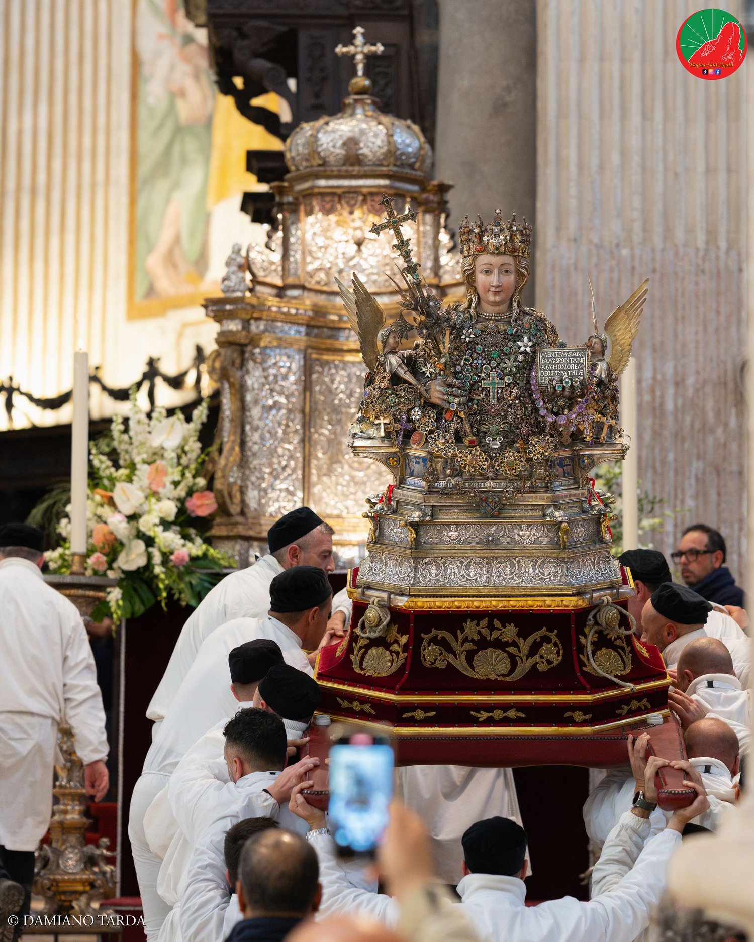 The bust of Saint Agatha carried on the shoulders of devotees in the Cathedral, among flowers and candles.