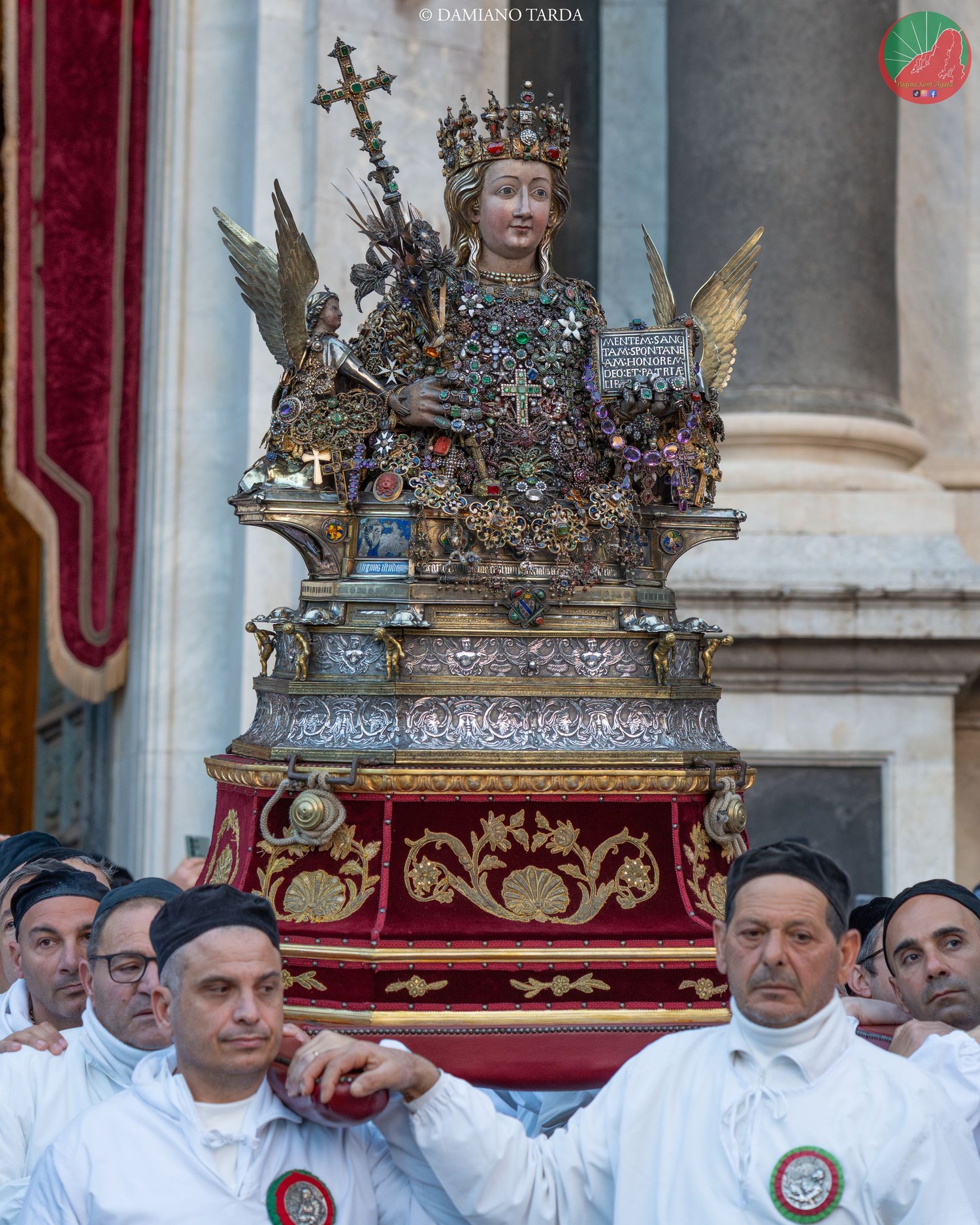 The reliquary bust of Saint Agatha carried by devotees in white robes at the entrance of the Cathedral.
