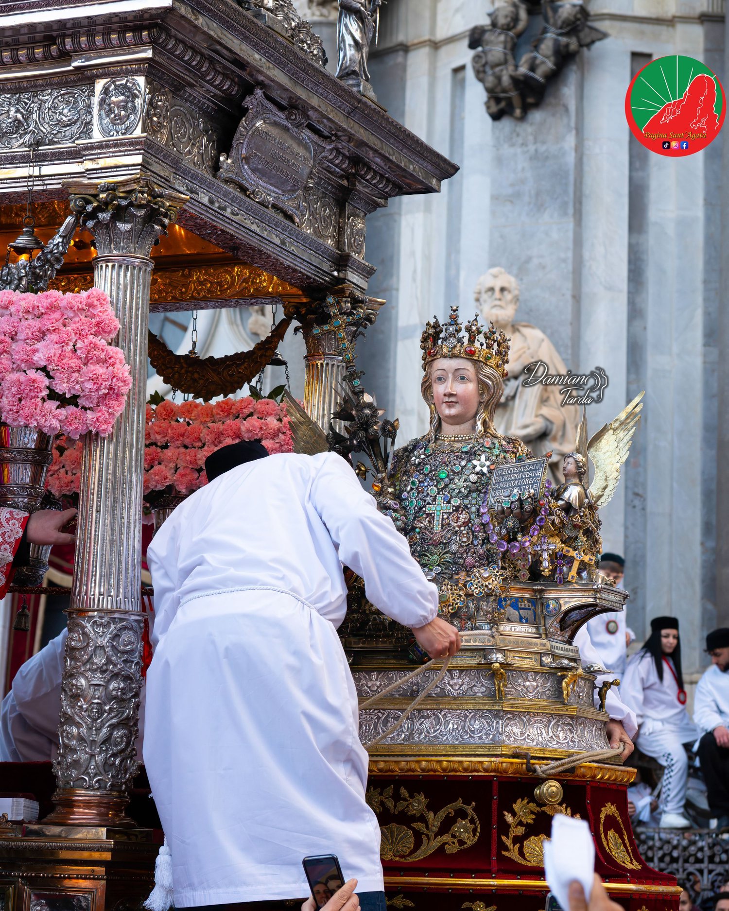 A devotee beside the bust of Saint Agatha on the fercolo decorated with pink carnations.